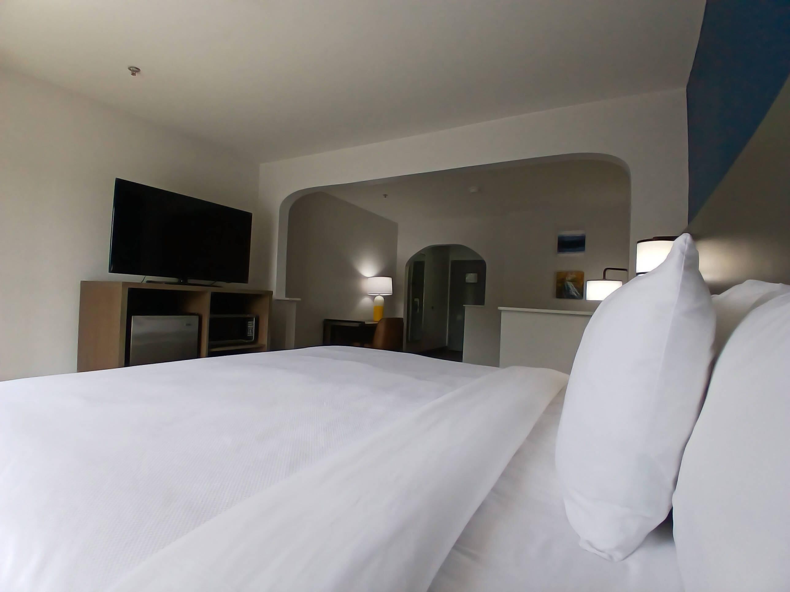 A hotel room with a bed, a television, a microwave, and a desk with a lamp.