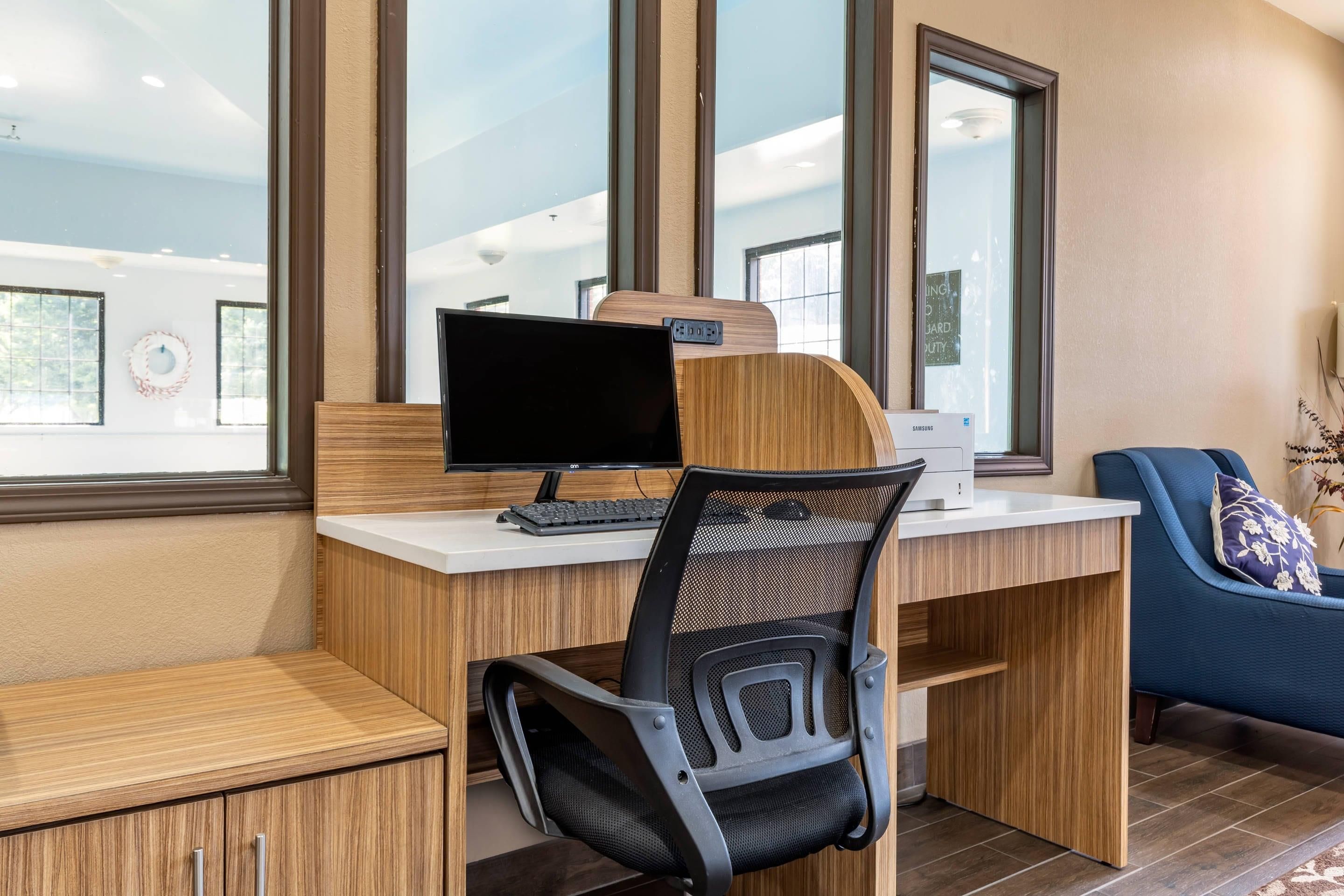 A modern office space with a wooden desk, a computer, a mesh chair, and a blue sofa.