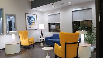 Eine moderne Lobby mit zwei gelben Sesseln, einem blauen Sofa, einem runden Tisch und einer Stehlampe.