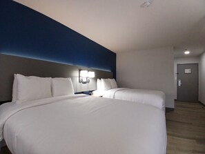 A hotel room with a large bed, two bedside tables, a nightstand, and a wall-mounted lamp.