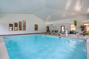 An indoor swimming pool with clear water, a diving board, and lounge chairs.