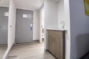 A hallway with a grey door, a white wall, and a wooden cabinet with a sink. - Comfort Inn Marion near Downtown & Blue Ridge PKWY (Marion)