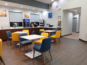 A modern restaurant with a counter, yellow and blue chairs, and a coffee machine.