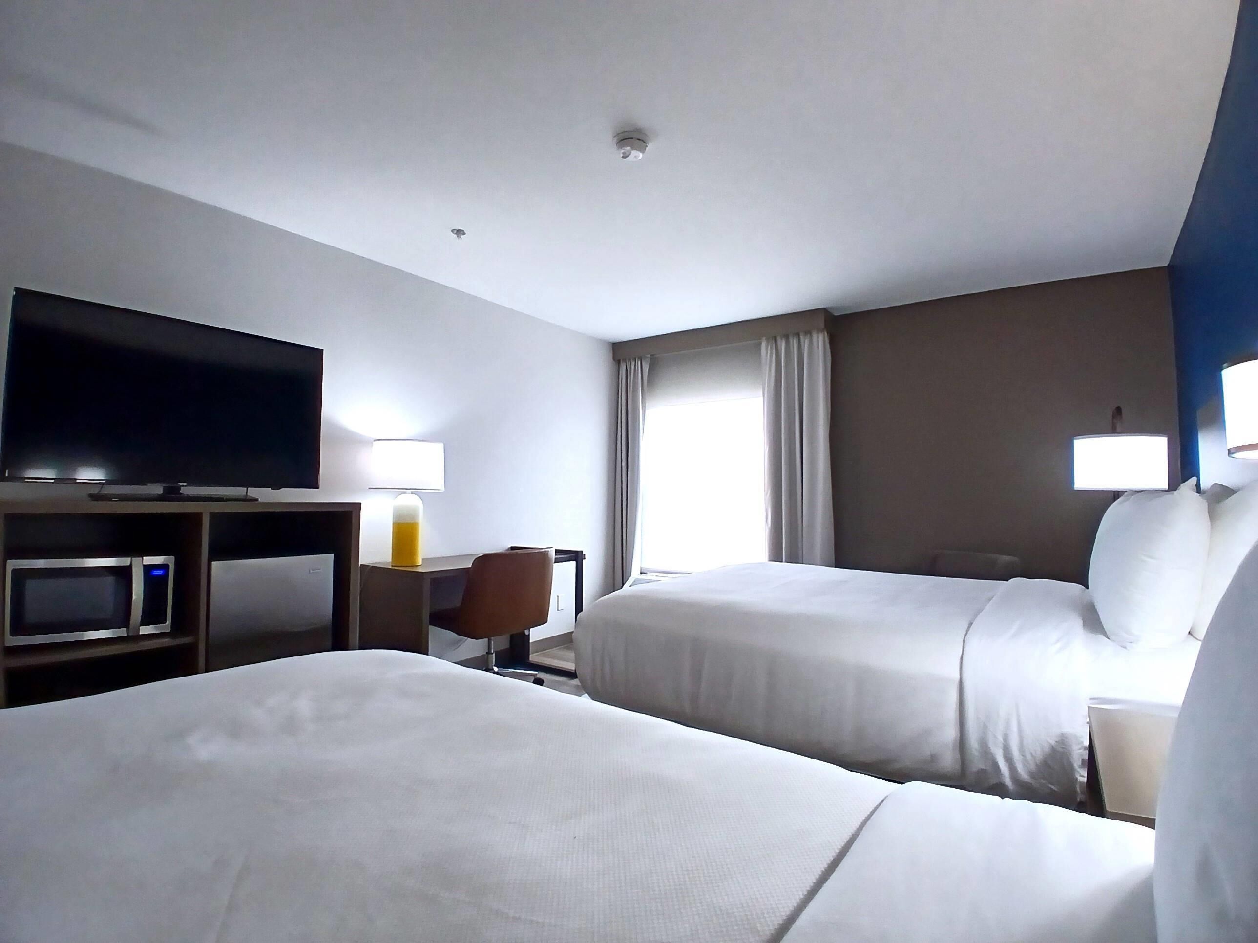 Habitación de hotel con dos camas, un televisor de pantalla plana, un escritorio con lámpara, microondas y ventana con cortinas.