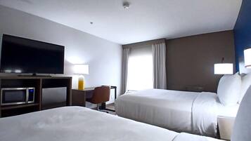 Habitación de hotel con dos camas, un televisor de pantalla plana, un escritorio con lámpara, microondas y ventana con cortinas.