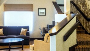 A modern living room with a sofa, armchair, and coffee table. A staircase with a patterned carpet leads to an upper floor. - Sleep Inn Florence North (Florence)
