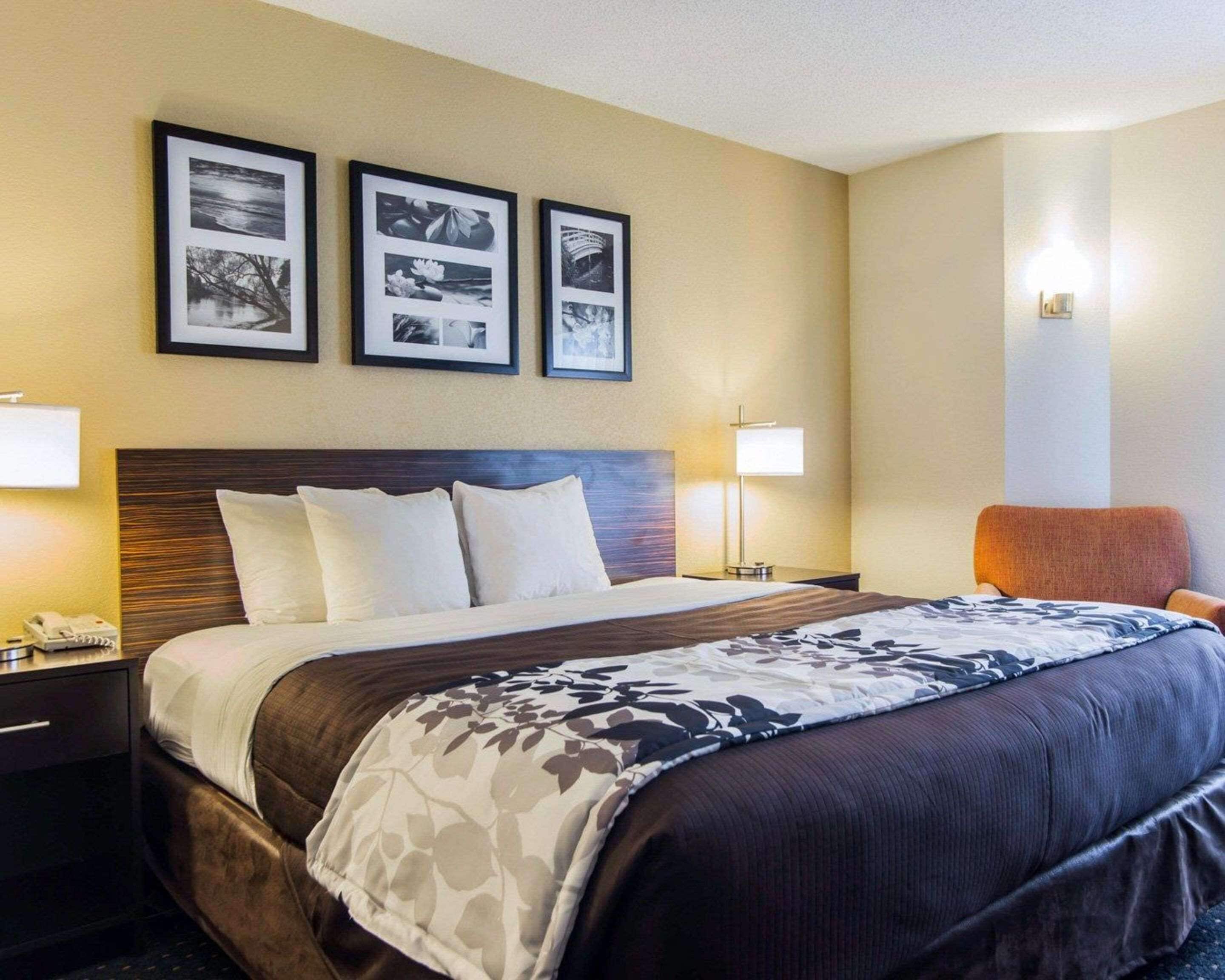 A hotel room with a large bed, two bedside tables, a nightstand, a chair, and three framed pictures on the wall.