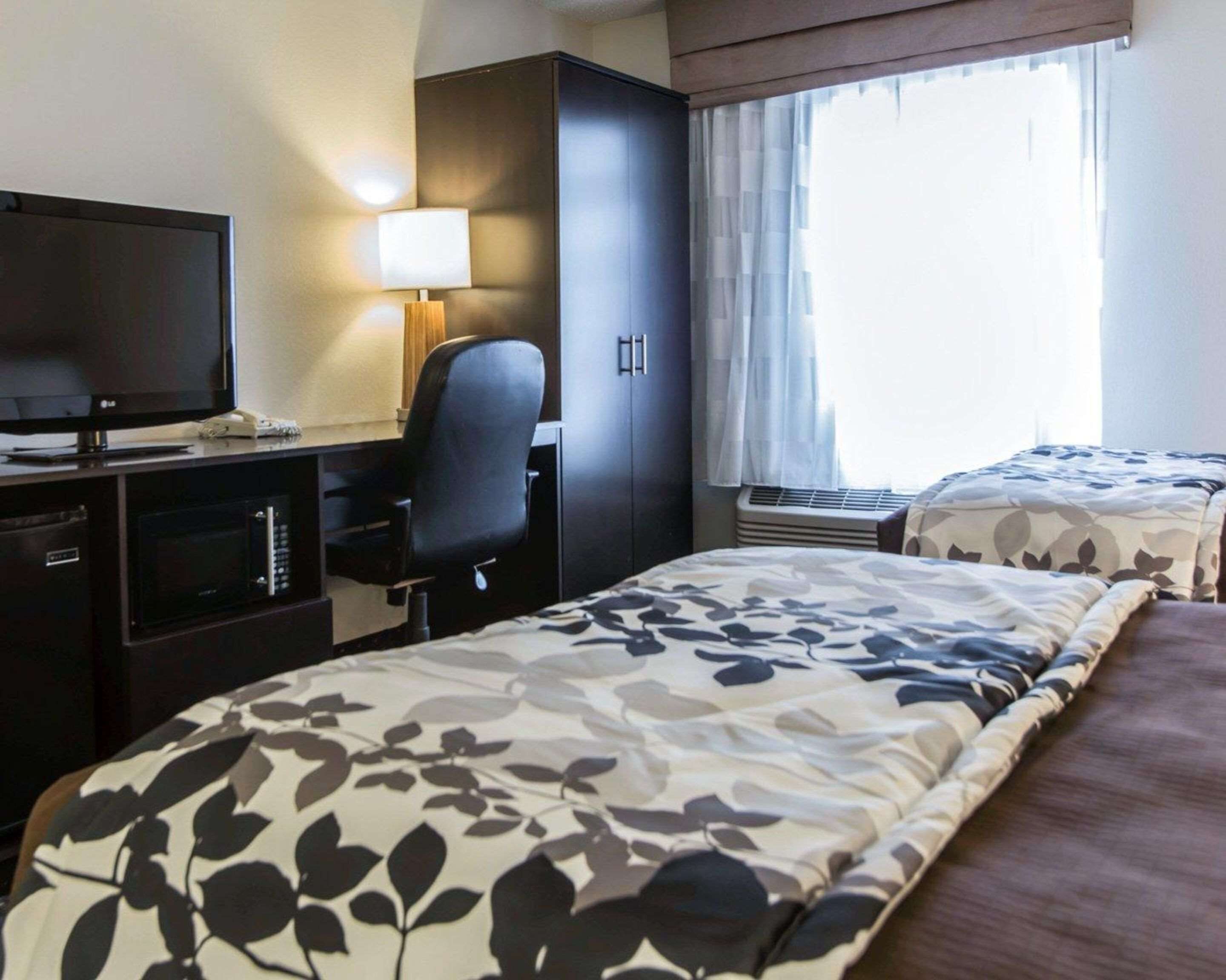 A hotel room with a bed, a desk with a computer, a TV, and a window with curtains.
