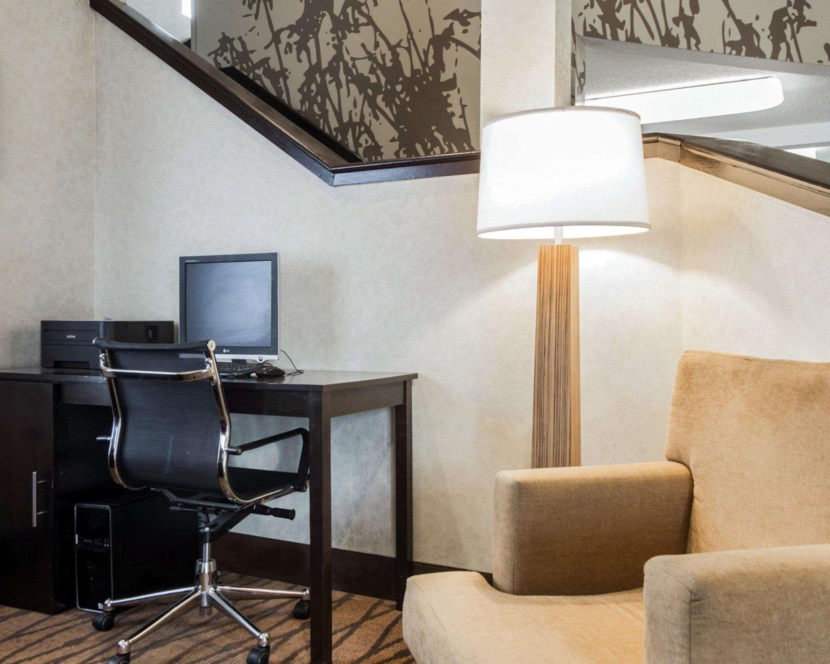 A hotel room with a desk, a computer, a chair, a lamp, and a sofa.