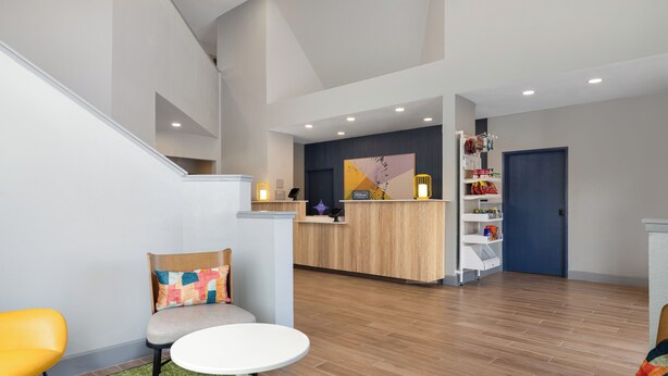 A reception area with a wooden reception desk, a small seating area with a round table, and a staircase leading to an upper level. - Spark by Hilton El Paso University (El Paso)