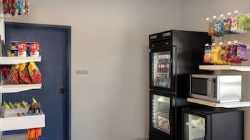 Une petite cuisine équipée d’un réfrigérateur, d’un four à micro-ondes et d’étagères remplies de collations et de boissons.