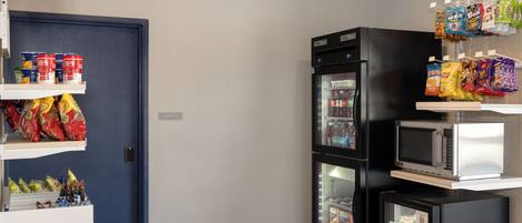 Una kitchenette compacta con refrigerador, microondas y estantes llenos de aperitivos y bebidas.