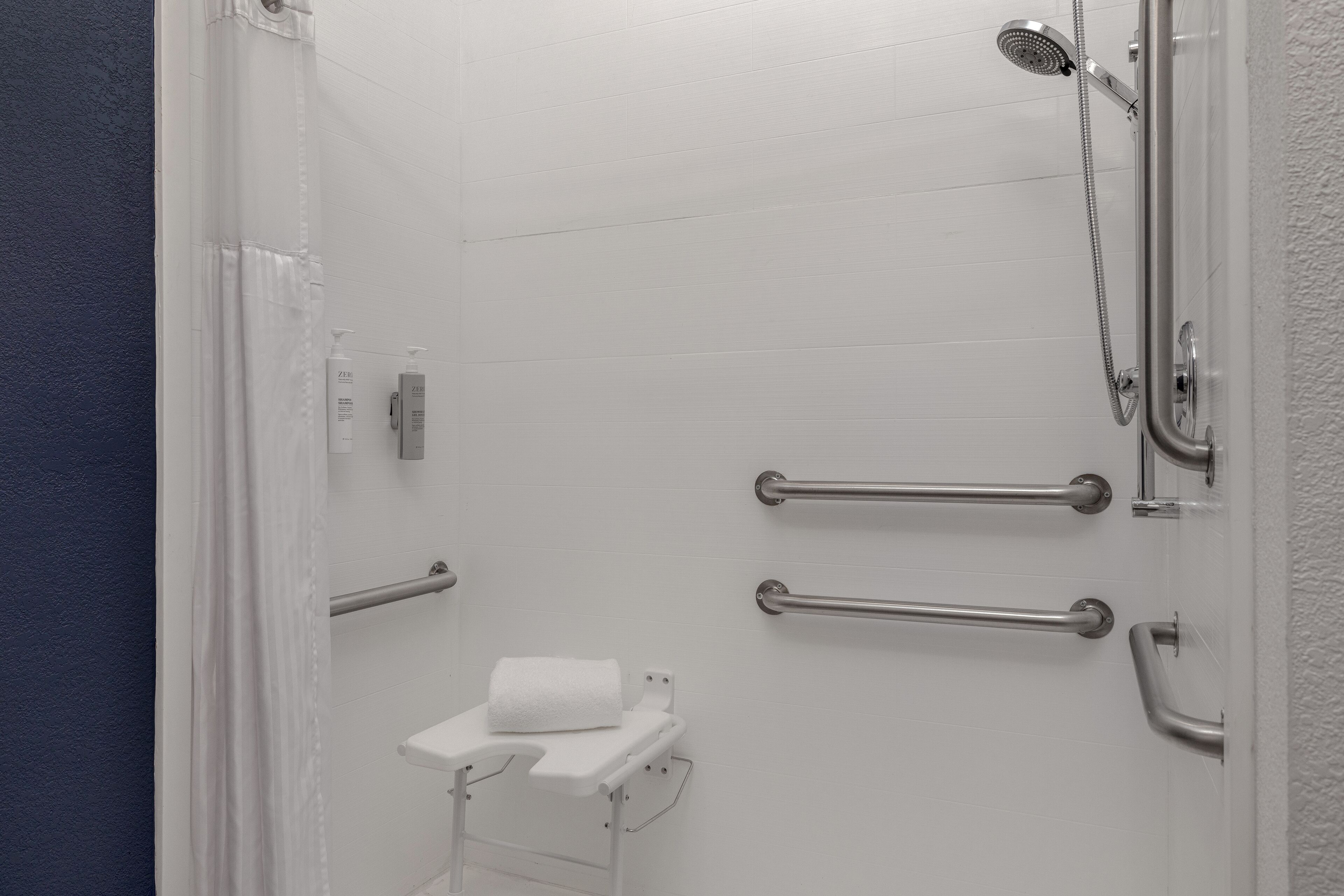 A bathroom with a shower, grab bars, a toilet, and a towel rack.
