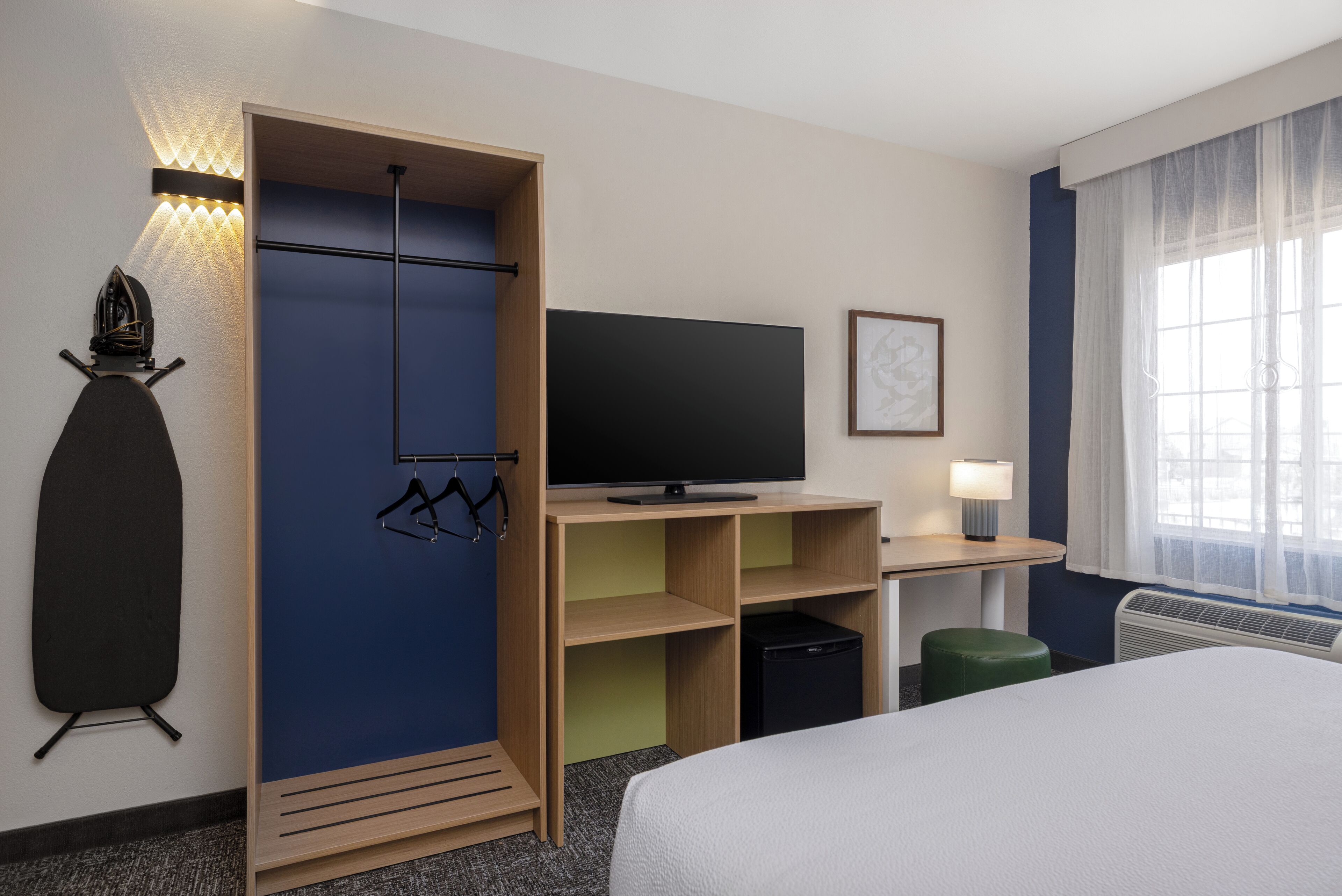 A hotel room with a bed, a television, a desk with a chair, a wardrobe, and a window with curtains.