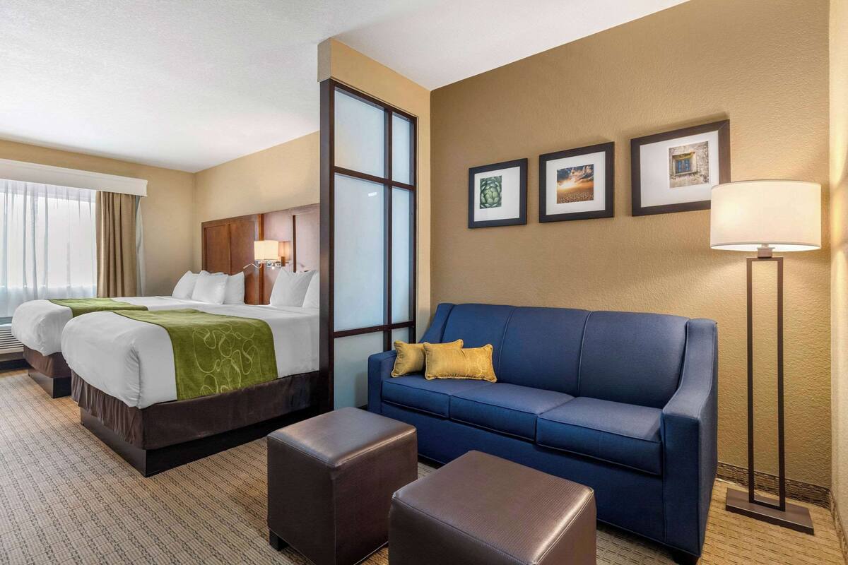 A hotel room with a large bed, a blue sofa, and two armchairs. There are framed pictures on the wall and a floor lamp.