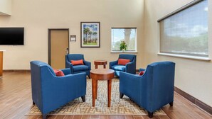 Un vestíbulo con sillones azules, una mesita de madera, un televisor de pantalla plana en la pared y una ventana con vistas a palmeras.