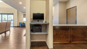 Un hall de hotel con mostrador de recepción, un televisor y una impresora Samsung.