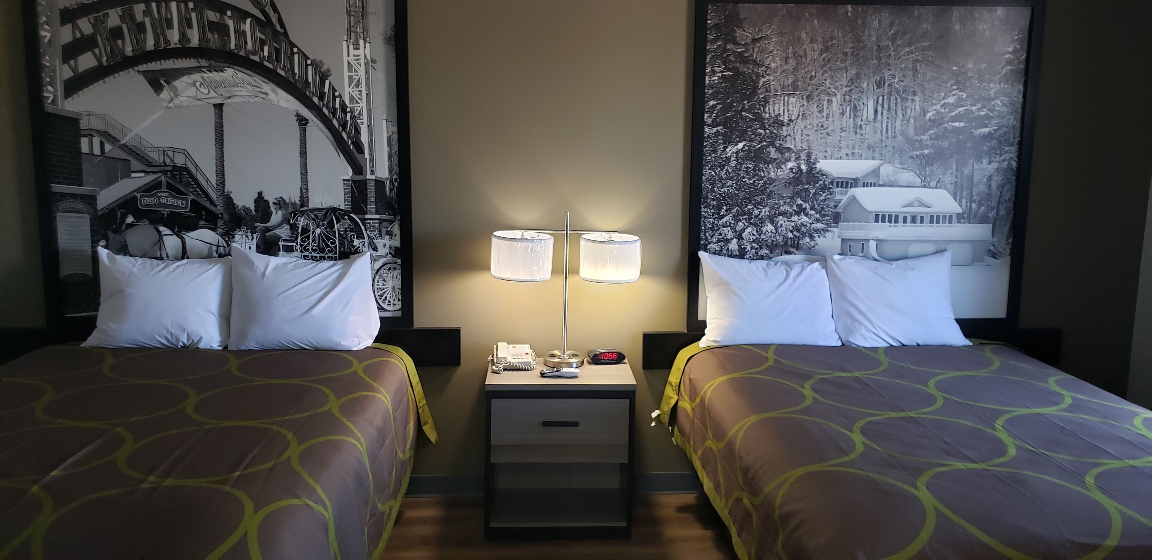 A hotel room with two beds, a nightstand with a lamp, a clock, and a framed picture on the wall.