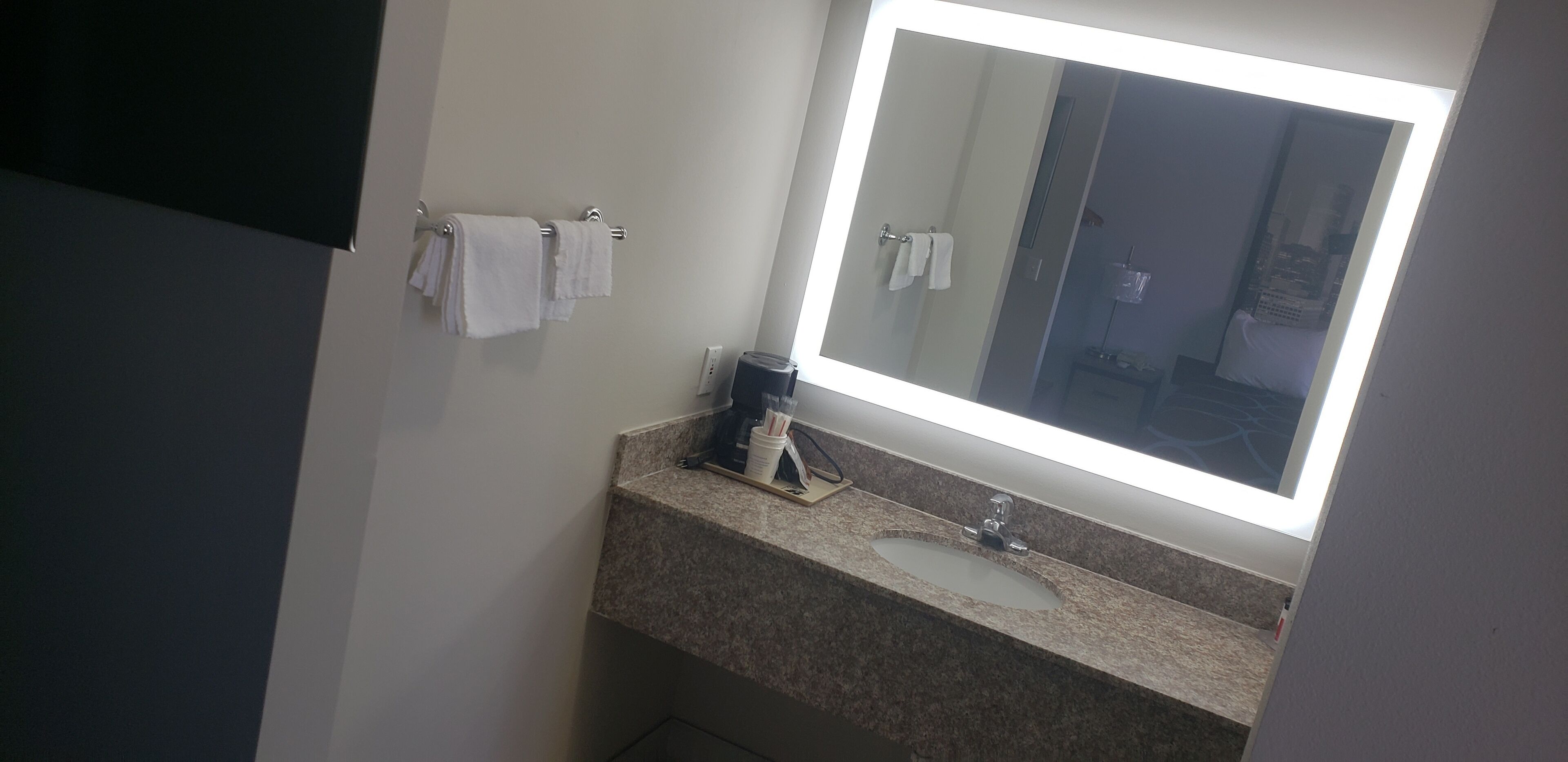 Un baño con encimera de granito, un lavabo, un espejo y dos toallas colgadas en un perchero.