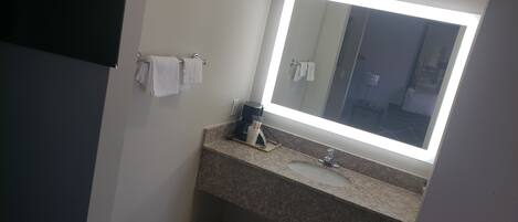 Un baño con encimera de granito, un lavabo, un espejo y dos toallas colgadas en un perchero.