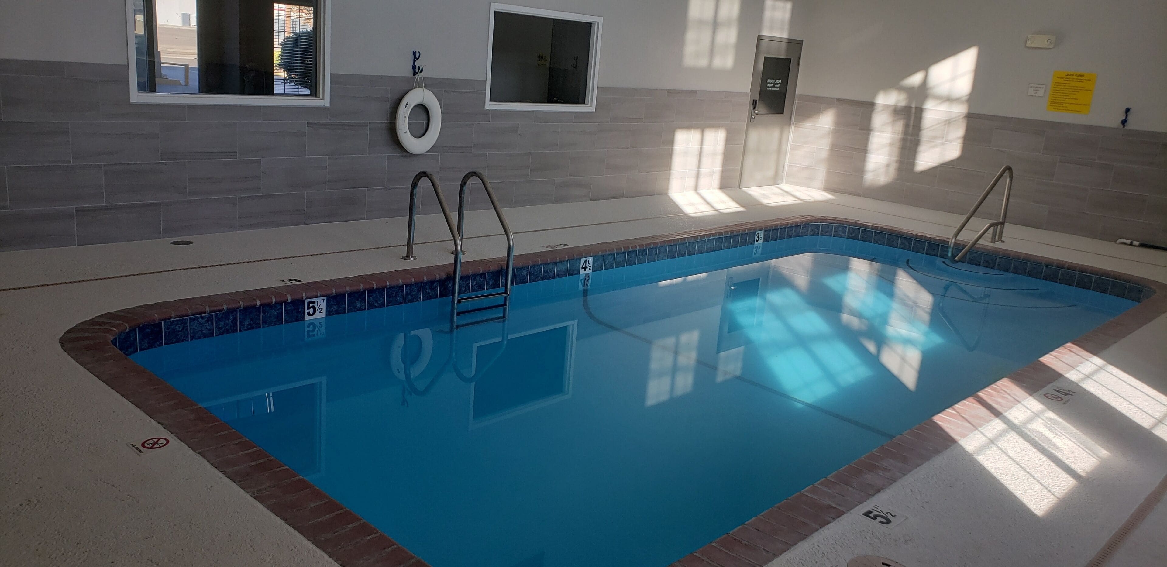 An indoor swimming pool with clear water, marked lanes, and a tiled wall.