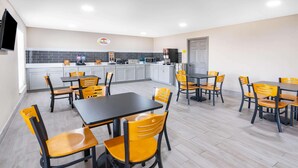 Een eethoek met tafels en stoelen, een keuken op de achtergrond en een deur.