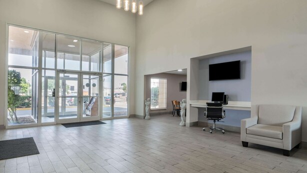 Een ruime lobby met een grote glazen deur, een wandgemonteerde flatscreen-tv, een bureau met stoel en een bank.