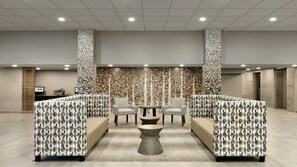 A modern lobby with patterned seating, a central coffee table, and a decorative wall. - Holiday Inn Express Williamsbrg Busch Gardens Area by IHG (Williamsburg)