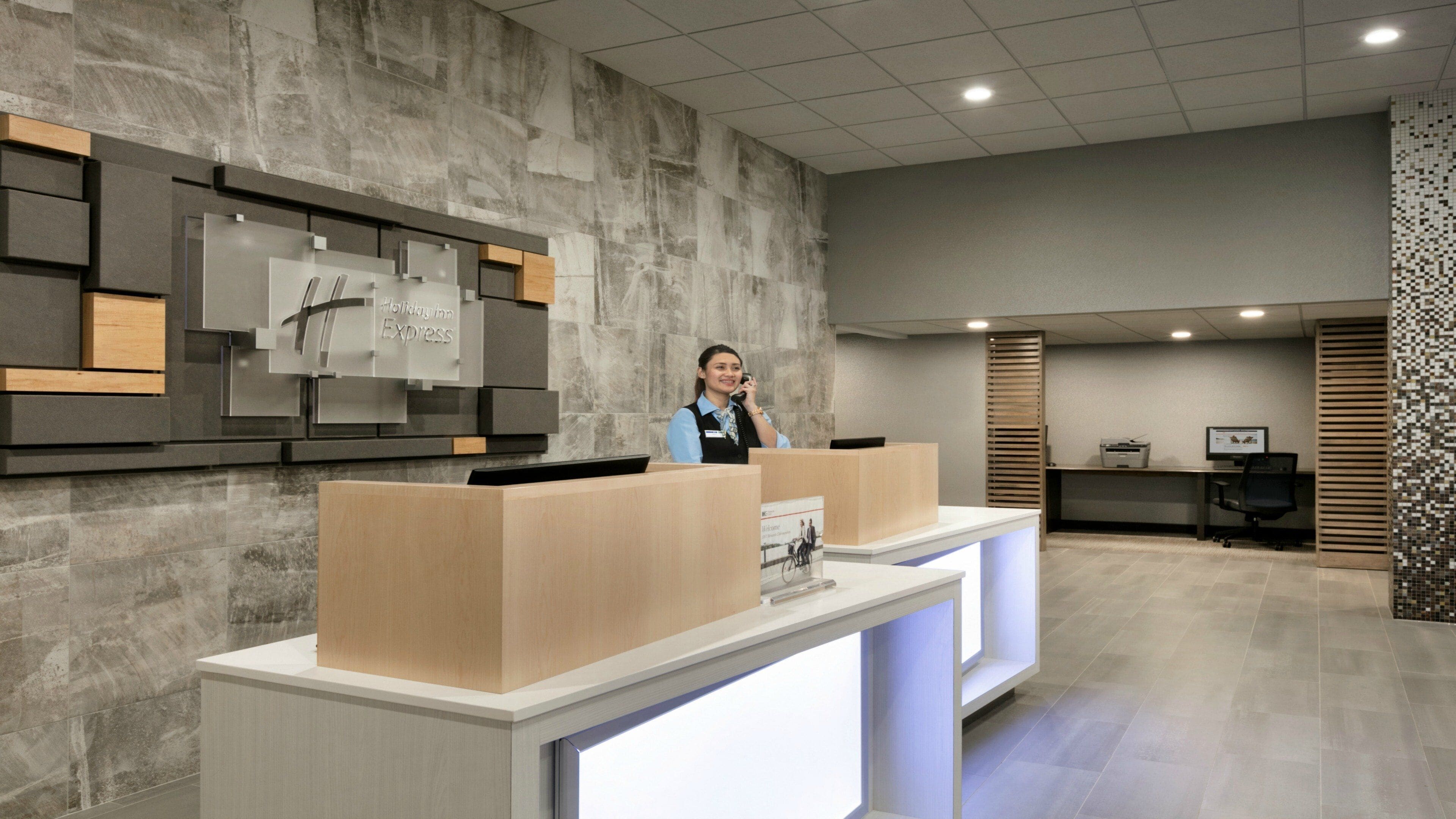 A hotel reception desk with a modern design, a receptionist, and a computer monitor.