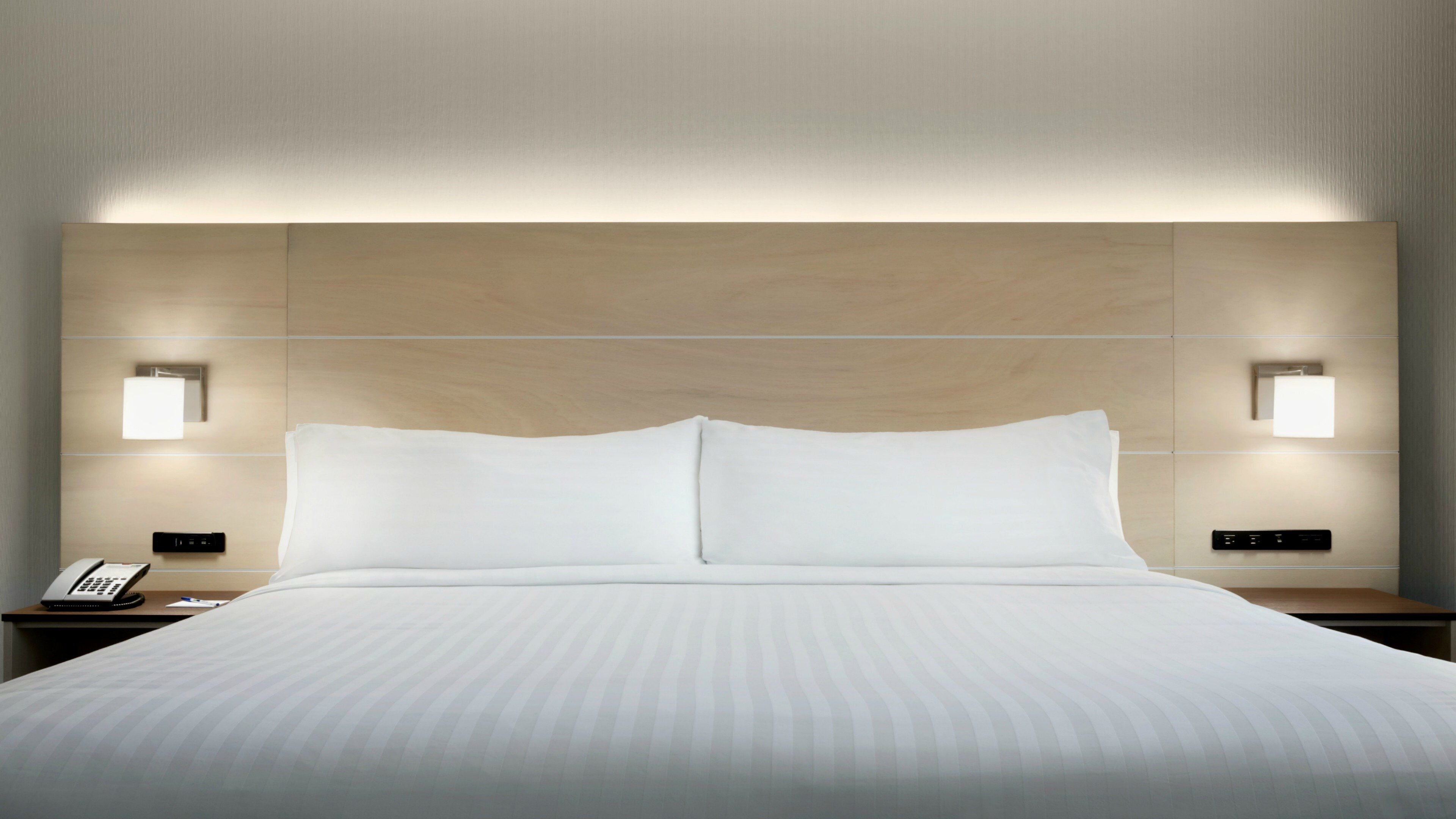 Une chambre d’hôtel avec un grand lit, deux tables de chevet, un téléphone fixé au mur et deux lampes fixées au mur.