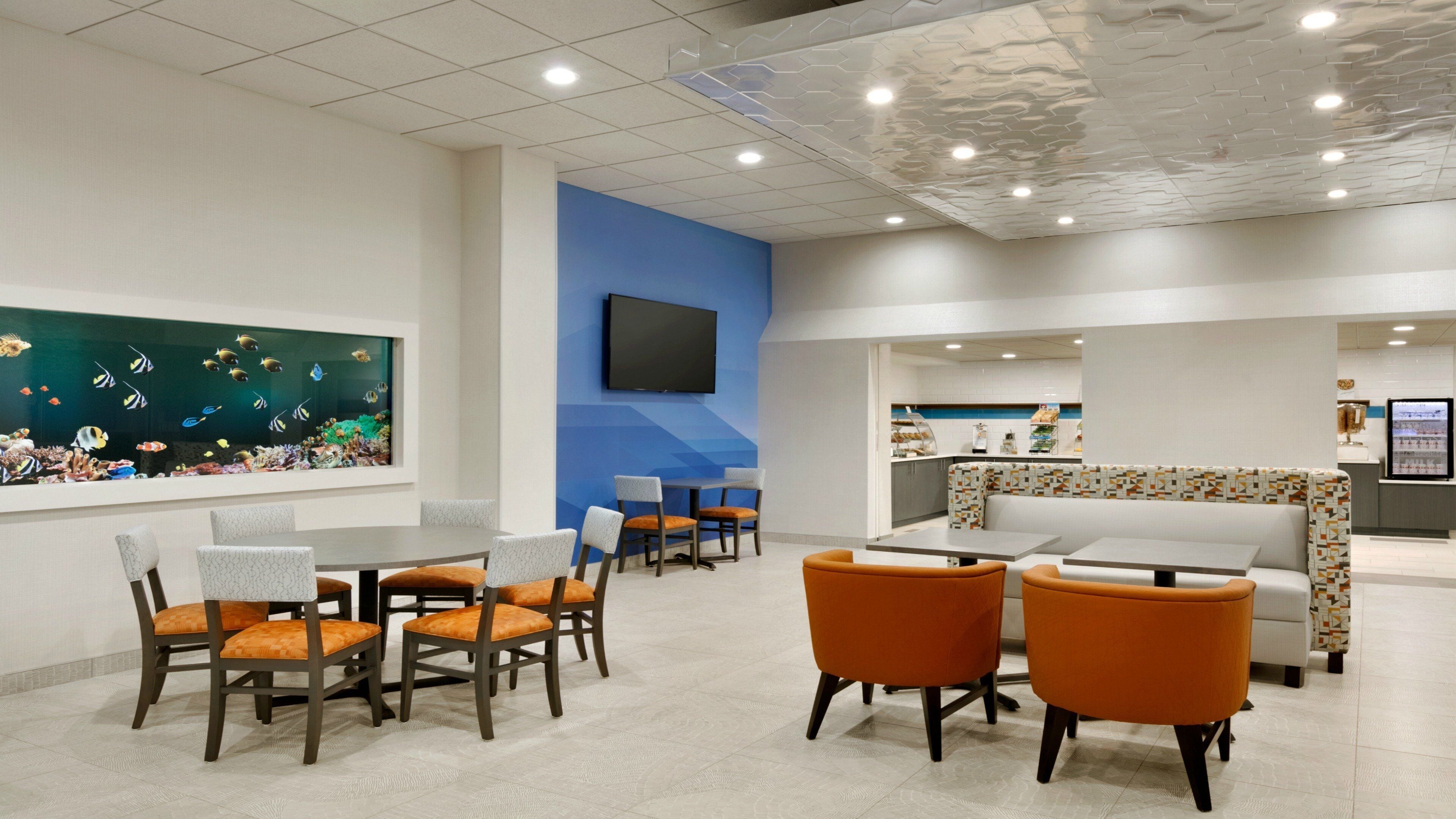 A restaurant with a blue accent wall, a fish tank, and a seating area with orange chairs.