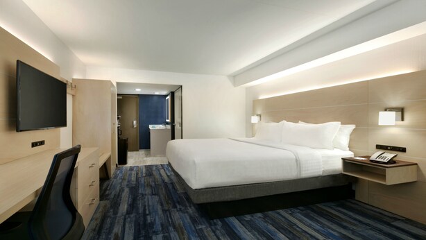 A hotel room with a large bed, a desk with a chair, a TV mounted on the wall, and a bedside table with a phone. - Holiday Inn Express Williamsbrg Busch Gardens Area by IHG (Williamsburg)
