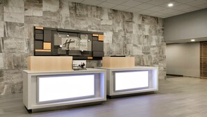 Aula, jossa on kiviseinä taustalla, digitaalinen näyttö ja puinen vastaanottotiski.