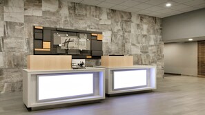 A reception area with a stone wall backdrop, a digital display, and a wooden reception desk. - Holiday Inn Express Williamsbrg Busch Gardens Area by IHG (Williamsburg)