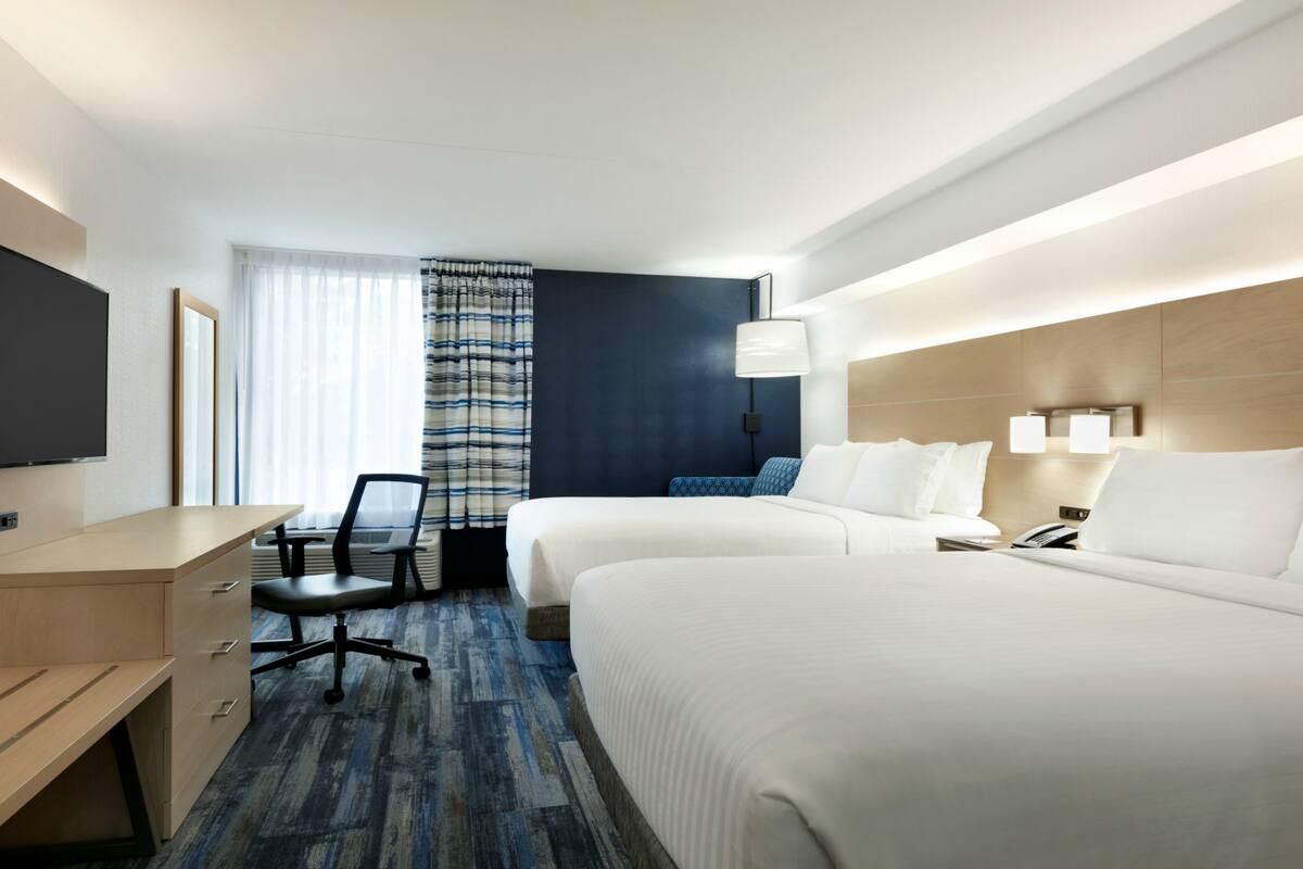 A hotel room with two beds, a desk, a chair, a TV, and a window with curtains.