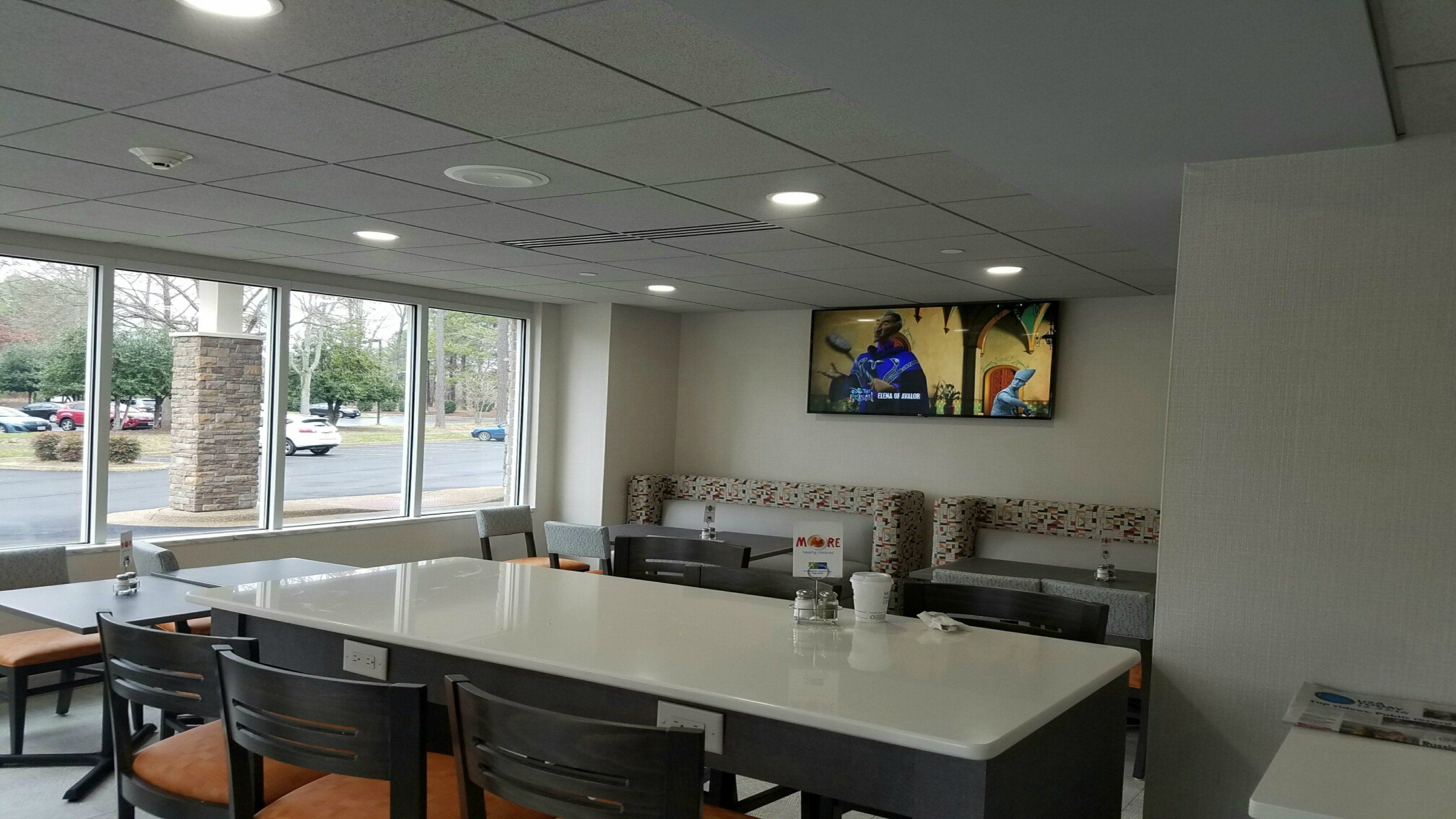 A restaurant with a large island table, booths, and a TV screen displaying a show.