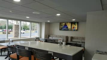 A restaurant with a large island table, booths, and a TV screen displaying a show.