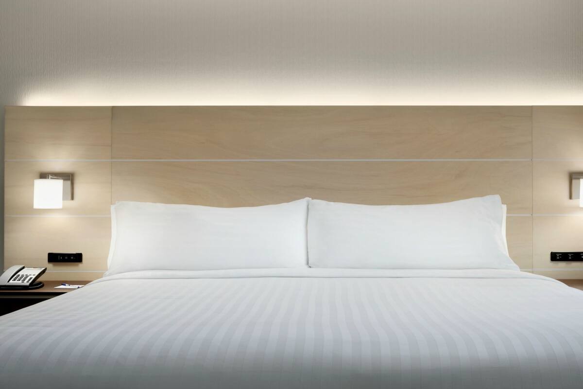 A hotel room with a large bed, two bedside tables, a nightstand, and wall-mounted lighting.