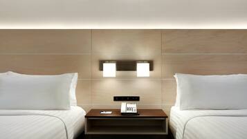 A hotel room with two beds, a nightstand with a phone, and wall-mounted lighting.