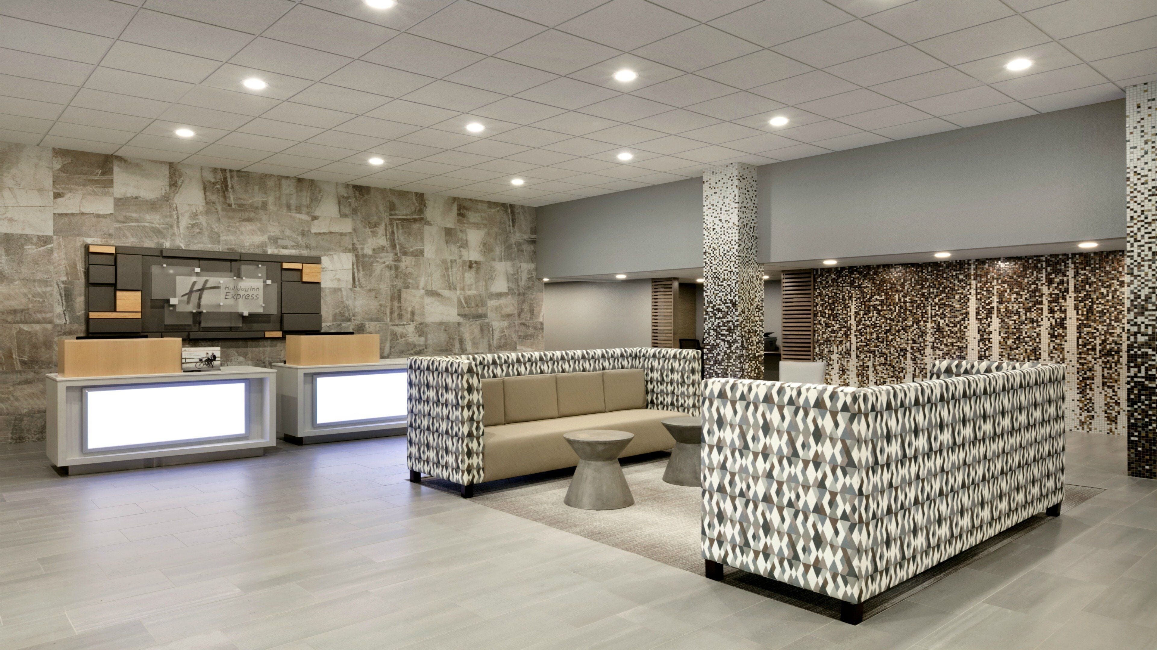 A hotel lobby with a reception desk, seating area, and a patterned wall.