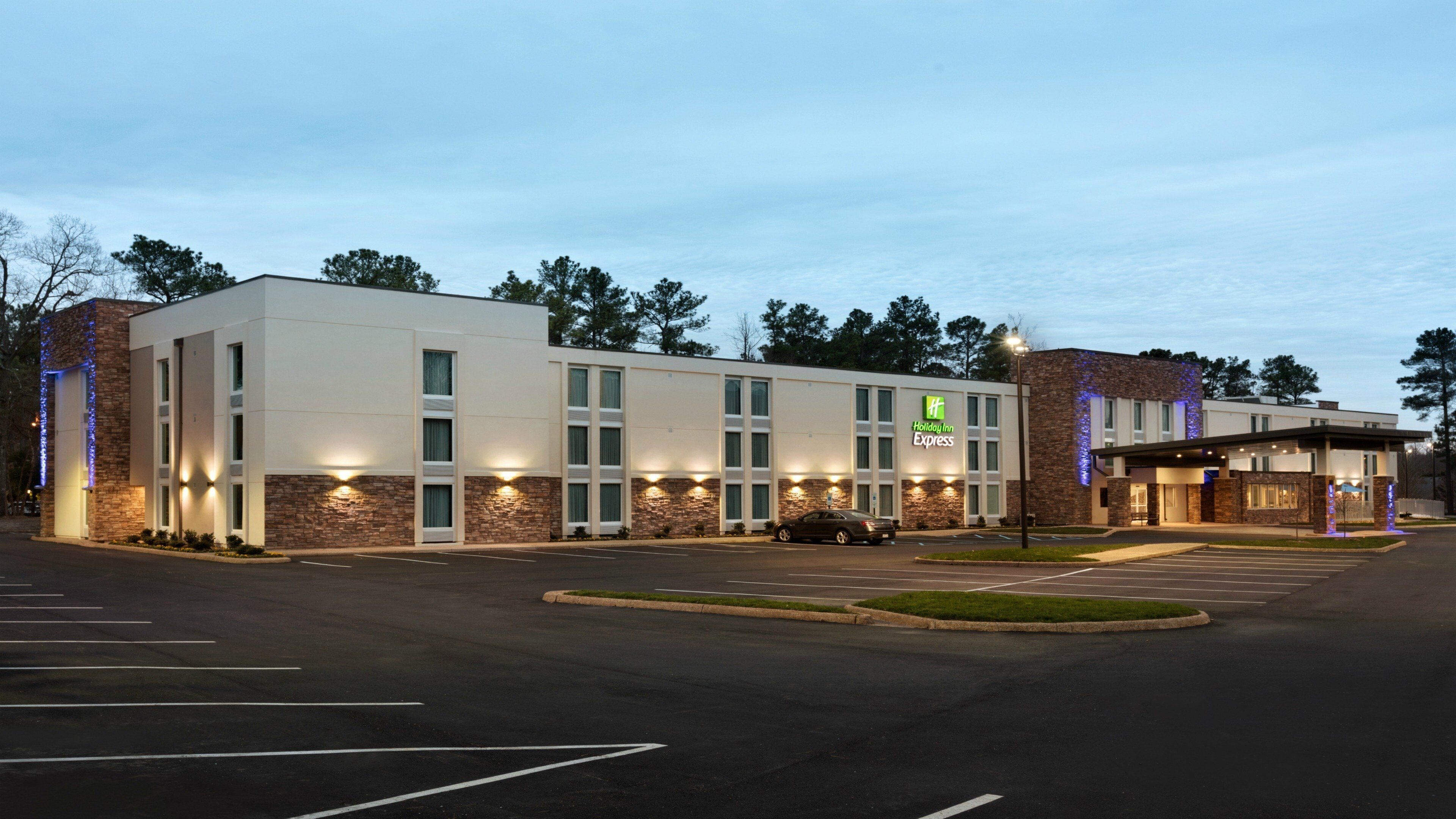 Un hôtel Holiday Inn Express doté d’un parking et dont la façade est agrémentée d’éléments en pierre et d’une enseigne lumineuse.