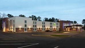 A Holiday Inn Express hotel with a parking lot and a building facade featuring stone accents and illuminated signage. - Holiday Inn Express Williamsbrg Busch Gardens Area by IHG (Williamsburg)