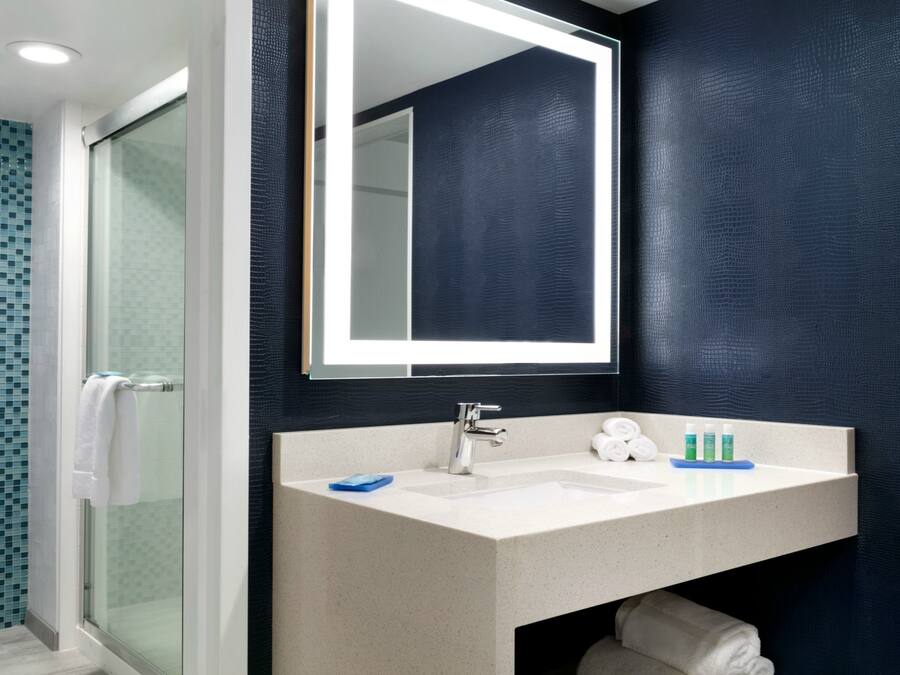 Een badkamer met een douchecabine van glas, een witte wastafel en een spiegel erboven.