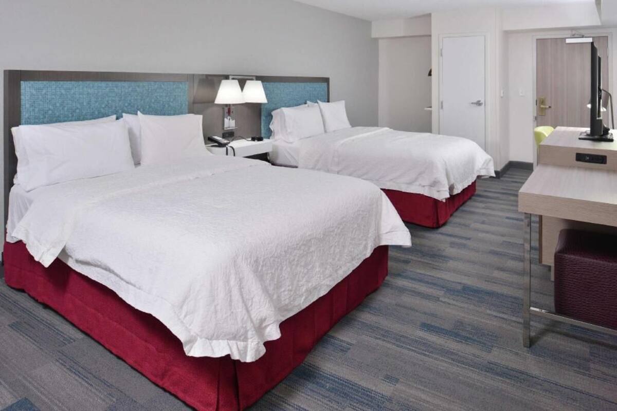 Une chambre d’hôtel avec deux lits, un bureau, une chaise, une lampe et une porte.
