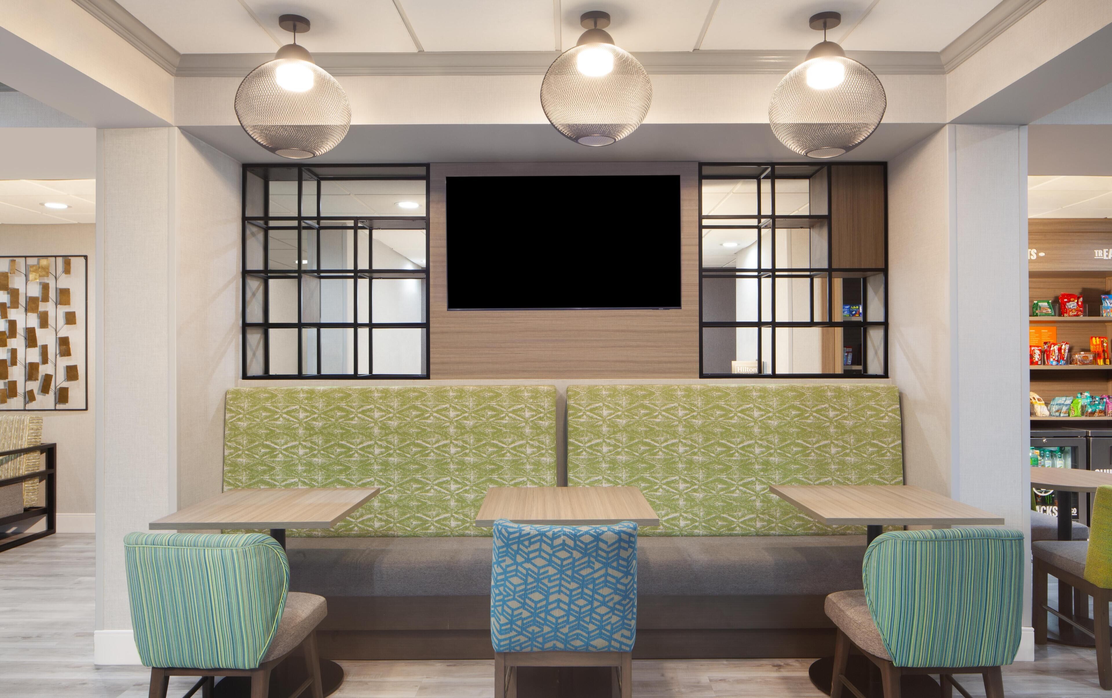 A seating area with two tables and chairs, a large flat-screen TV mounted above, and a patterned wall.
