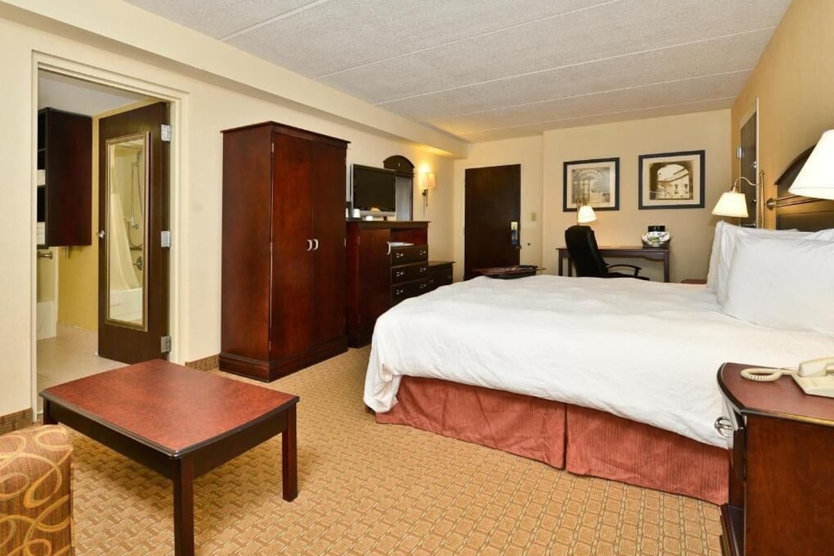 A hotel room with a bed, a desk, a chair, a wardrobe, and a small table.