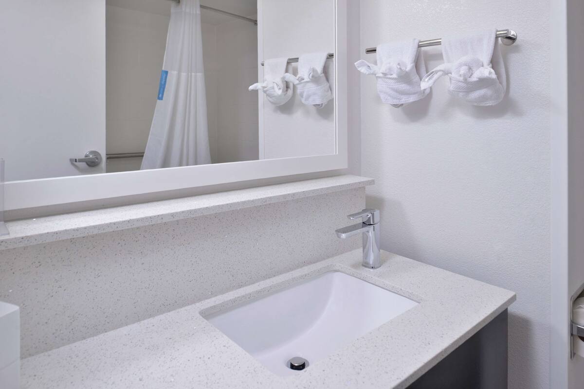 Une salle de bain avec un lavabo blanc, un miroir et deux serviettes suspendues à un porte-serviettes.