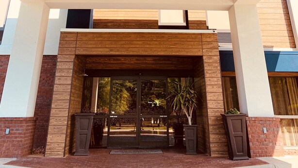 Ein moderner Gebäudeeingang mit Holzboden, Glasüren und einer Ziegel fassade.
