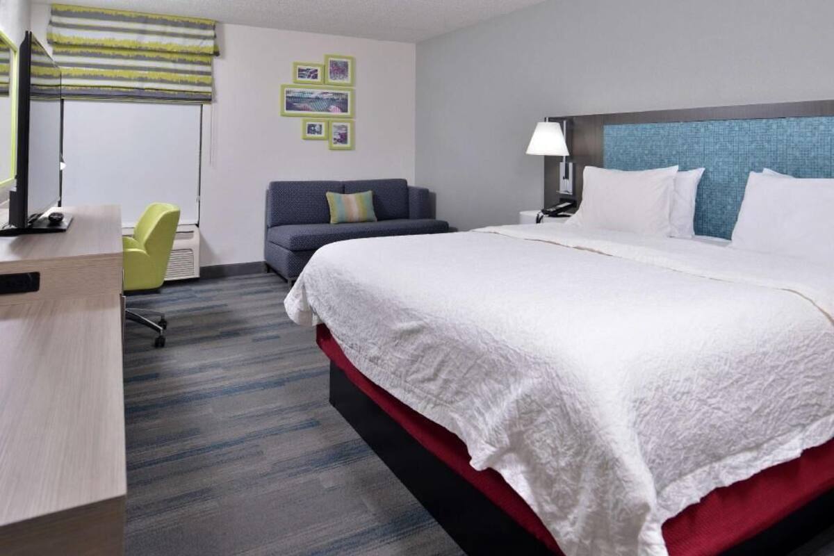 Une chambre d’hôtel avec un lit, un bureau, une chaise, une lampe et un mur décoré de tableaux.