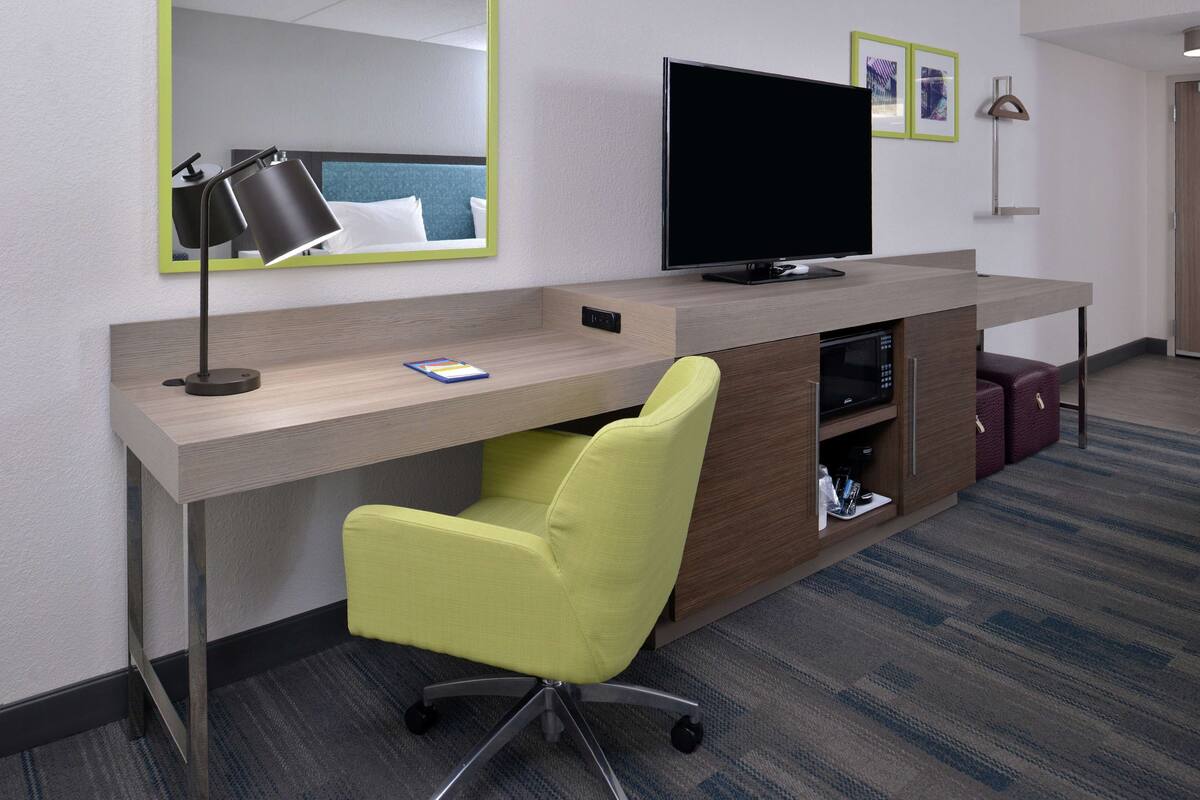 Une chambre d’hôtel équipée d’un bureau, d’une télévision, d’un miroir et d’une chaise.